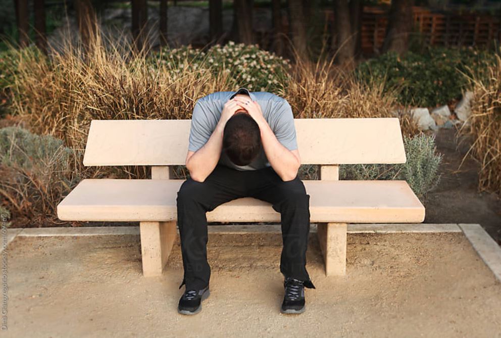 man sitting on a bench with his head in his hands