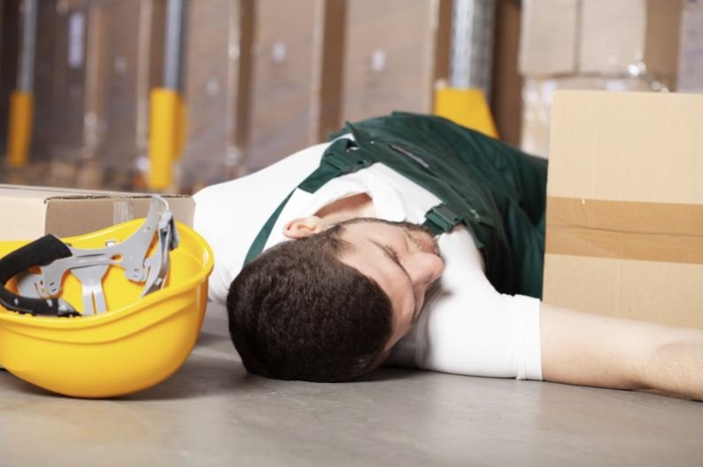 a man struck by a dropped object lies on the floor of a warehouse